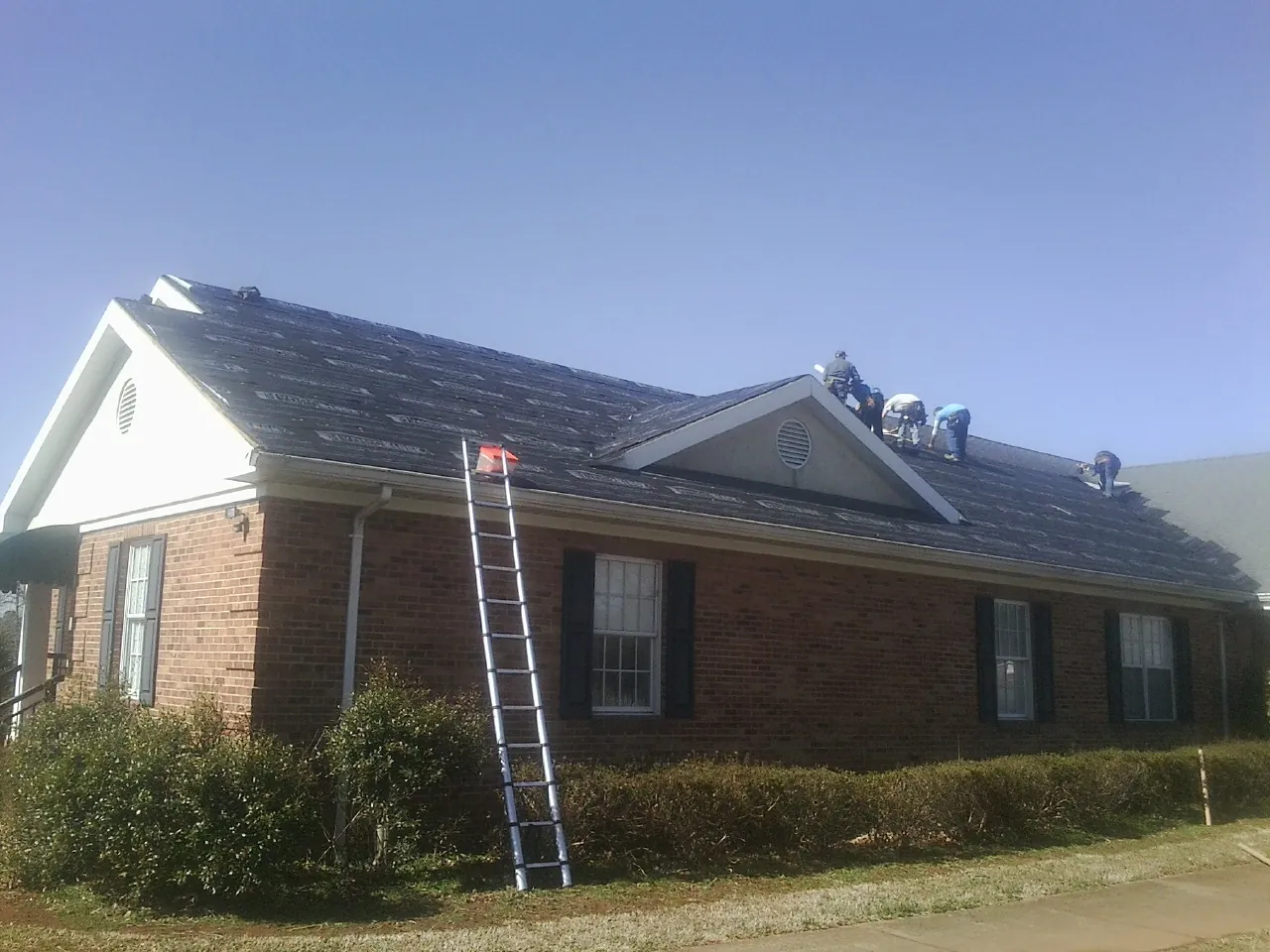 Crew tearing shingles off a brick ranch roof with a ladder set — Emergency Roof Repair work by our crew in Copenhagen