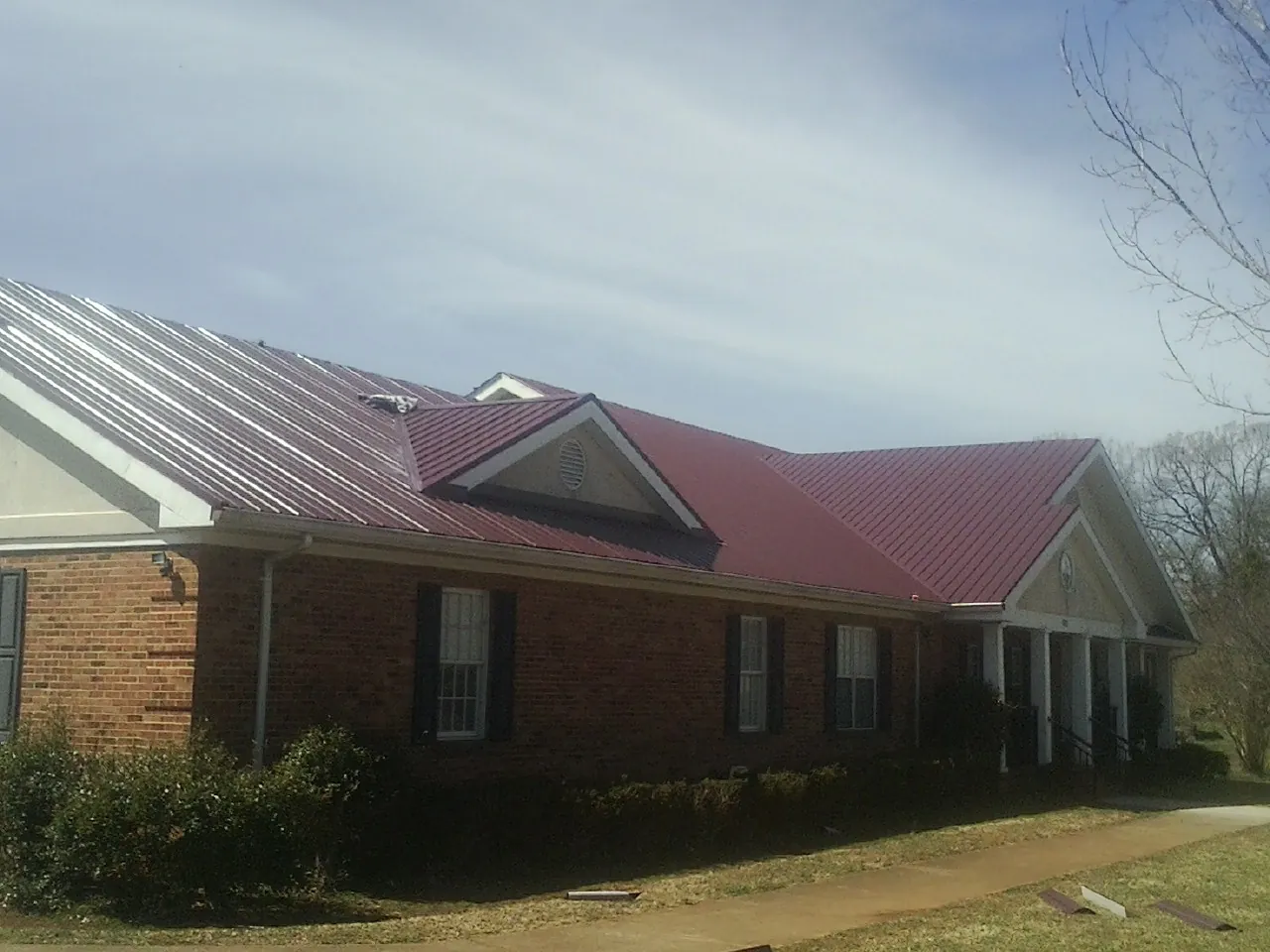 Red metal roof with gabled entries on a long brick building, from a Hail Damage Roof Repair job in Copenhagen